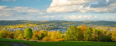 Landschaft mit Kleinstadt, bunten Bäumen, Wiesen, Windrädern